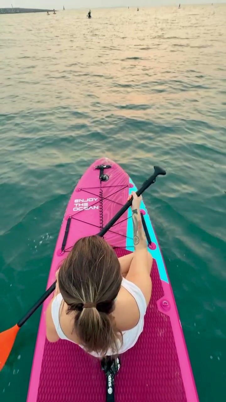 Overhead view of a paddler kneeling on a pink stand-up paddleboard at dusk
